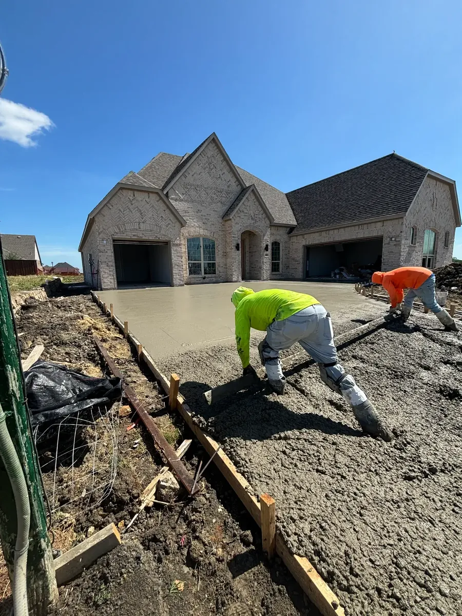 Crew members finishing a fresh concrete driveway in front of a brick home