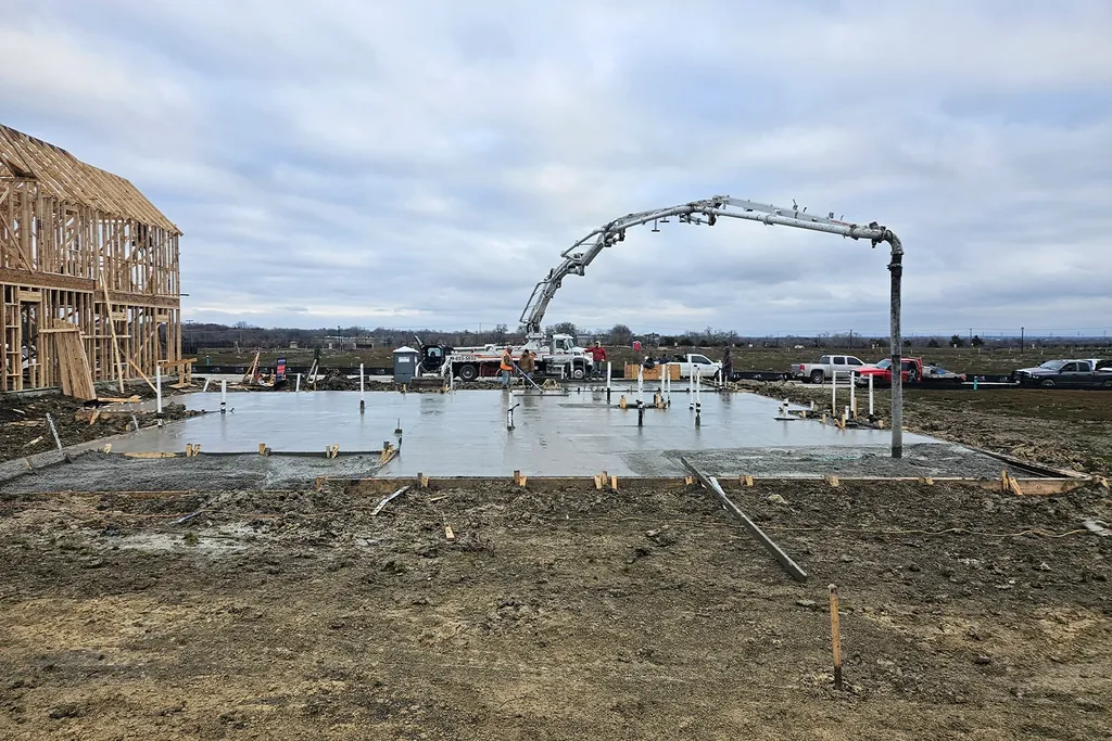 Concrete pump boom placing a foundation slab beside a framed house