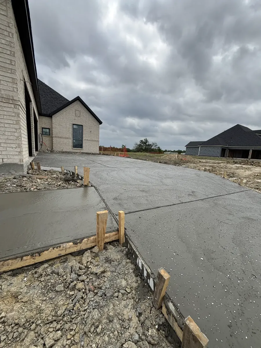 Freshly poured driveway with wood forms still in place beside a new home